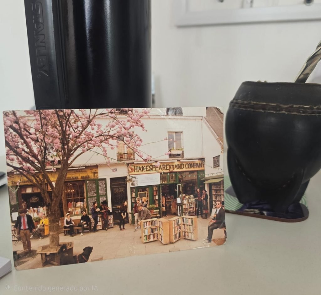 Postal de la librería Shakespeare and Company de París: un cerezo en flor, una guirnalda de luces, un grupo de gente sentada frente a la fachada y un perro